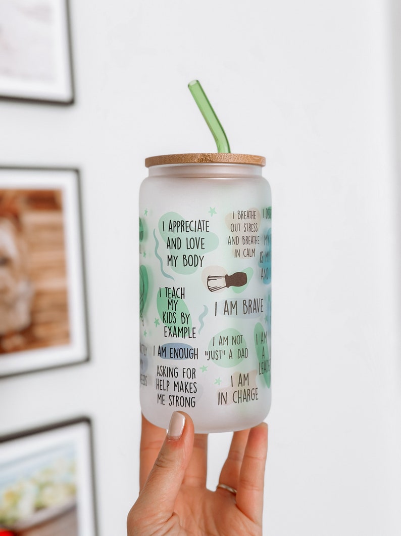 May include: A frosted glass water bottle with a bamboo lid and a green straw. The bottle has inspirational text printed on it, including "I appreciate and love my body", "I teach my kids by example", "I am brave", "I am enough", "I am not "just" a dad", "I am a leader", "Asking for help makes me strong", and "I am in charge".