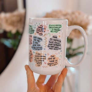 May include: White ceramic mug with colorful text and illustrations. The text includes bible verses and inspirational quotes. The mug has a handle on the right side.