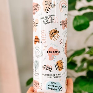 May include: White stainless steel tumbler with a colorful abstract design and motivational quotes. The quotes include "My feelings are valid", "I am loved", "Motherhood is not easy but I can do it", and "Love gives me strength".