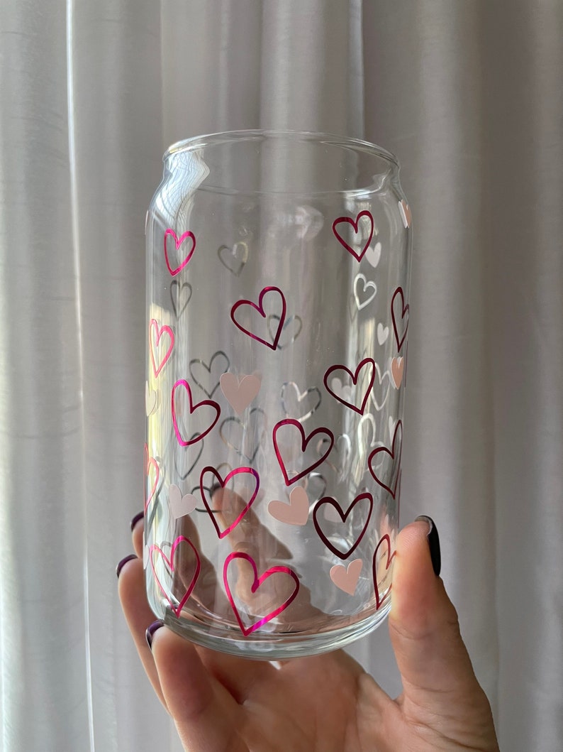May include: A clear glass can with a pink and white heart pattern. The can is perfect for holding beverages.