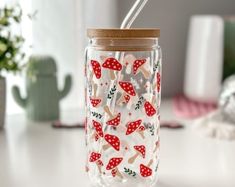 May include: A clear glass reusable water bottle with a bamboo lid and a straw. The bottle has a mushroom pattern with red and white mushrooms on a white background.