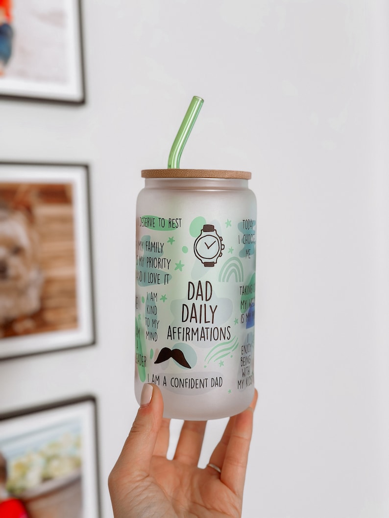 May include: A frosted glass tumbler with a bamboo lid and a green straw. The tumbler has a green, blue, and white design with the text "Dad Daily Affirmations" and "I am a confident dad".