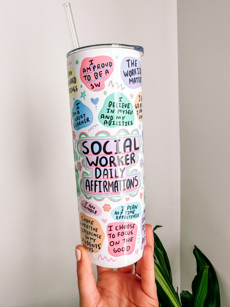 A white tumbler with a straw. The tumbler has colorful illustrations and text that reads 'Social Worker Daily Affirmations' and includes phrases like 'I am proud to be a SW', 'I believe in myself and my abilities', 'I make a positive difference in my students' lives', 'I choose to focus on the good', 'I plan my time effectively', and 'I am capable'.