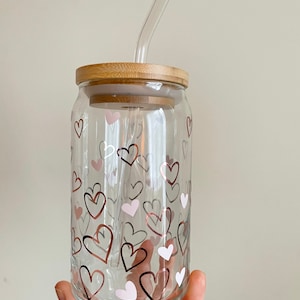 May include: A clear glass jar with a bamboo lid and a glass straw. The jar has a pattern of pink and gold hearts.