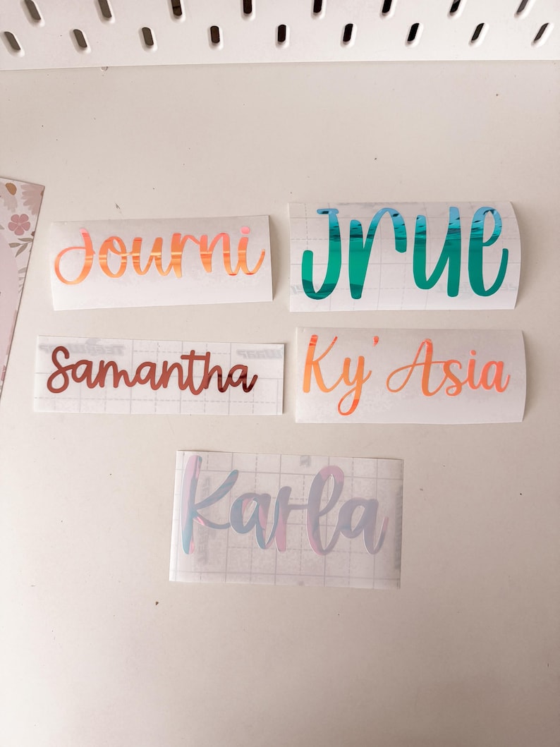 May include: Five custom vinyl name decals on transfer paper. The names include Journi in metallic copper, Jrue in metallic teal, Samantha in metallic bronze, Ky' Asia in metallic orange, and Karla in a multi-coloured pastel iridescent finish.