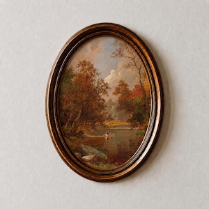 May include: An oval-shaped painting in a dark brown wooden frame depicting a landscape scene with autumn-colored trees, a calm river, and a small boat with figures on the water under a cloudy sky with soft light filtering through the foliage.
