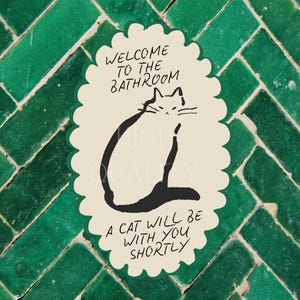 May include: An oval-shaped sticker with a scalloped edge featuring a cream background and a black line drawing of a cat. The text reads: WELCOME TO THE BATHROOM, A CAT WILL BE WITH YOU SHORTLY. The sticker has a dark green border.