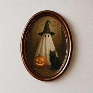 Puede incluir: Una pieza de arte mural con marco ovalado que representa a un fantasma blanco con un sombrero negro puntiagudo, junto a una calabaza naranja tallada y un gato negro. La escena se sitúa en un bosque oscuro con hojas caídas en el suelo.