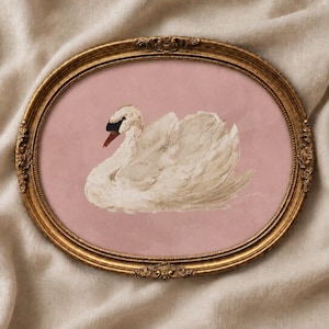 May include: An oval-shaped, ornate gold frame containing a print of a white swan with a black beak and eye detail. The swan is positioned against a solid, muted pink background, creating a contrast between the bird and the backdrop.
