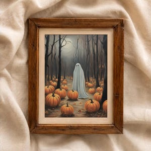 May include: A framed wall art print featuring a white ghost standing in a dark forest filled with orange pumpkins. The artwork is enclosed in a rustic brown wooden frame with a light-colored mat border, showcasing a scene with trees and a full moon.