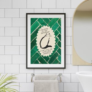 May include: A framed wall art print featuring a cream-colored scalloped oval with a black line drawing of a cat. The text reads: Welcome to the bathroom, a cat will be with you shortly. The background is a dark green, glossy, herringbone tile pattern.