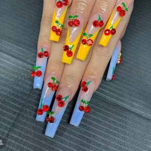 May include: Long, light blue and yellow acrylic nails with a cherry design. Each nail is decorated with a 3D cherry with a green stem and red fruit.