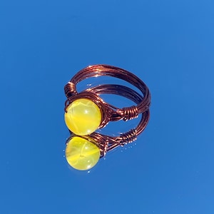 May include: A copper wire ring with a yellow gemstone. The ring is wrapped in copper wire and has a simple design.