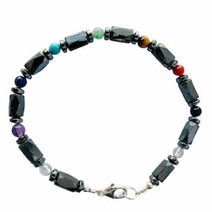 May include: A beaded bracelet featuring a variety of colorful gemstones and dark gray, faceted hematite beads. The bracelet includes a silver-colored clasp and is designed with a chakra theme.