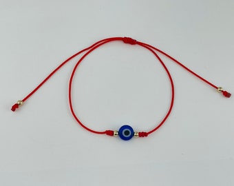 May include: Red string bracelet featuring a blue and white evil eye charm. The bracelet has adjustable sliding knots and small gold-colored beads. A simple, yet striking piece of jewelry.