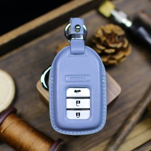 Puede incluir: Un llavero de cuero azul claro con un llavero plateado y cuatro botones. El llavero tiene la palabra "HONDA" grabada en la parte superior.