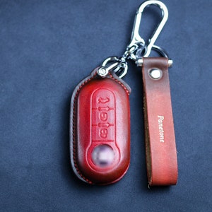 May include: A red leather key fob with a silver key ring and a brown leather strap with the word "Panettone" embossed on it.