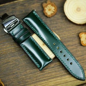 May include: A dark green leather watch strap with white stitching and a silver buckle.