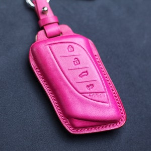 May include: A bright pink leather key fob with a stitched edge. The fob has four buttons with raised symbols.