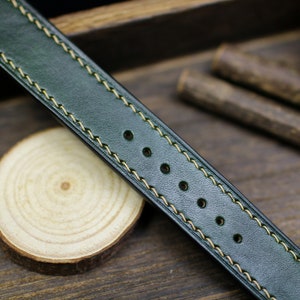 May include: A dark green leather watch strap with light yellow stitching. The strap has five holes for adjusting the size.