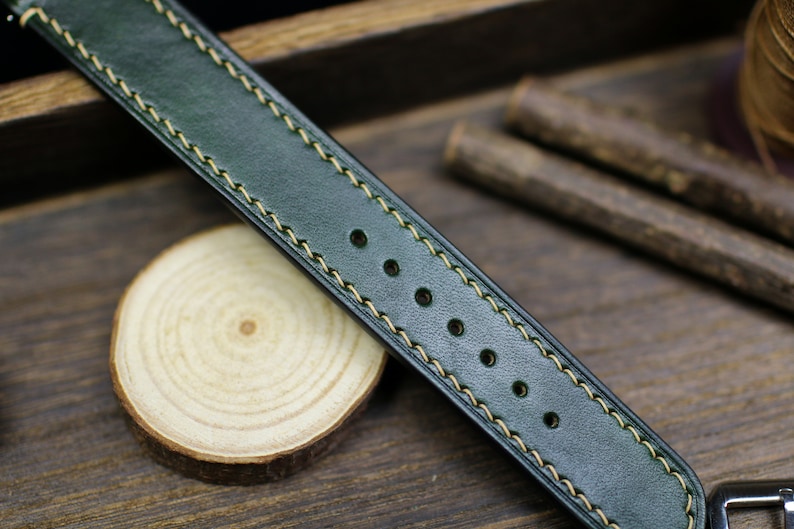 May include: A dark green leather watch strap with light yellow stitching. The strap has five holes for adjusting the size.