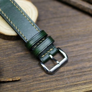 May include: A dark green leather watch strap with light brown stitching and a silver buckle.
