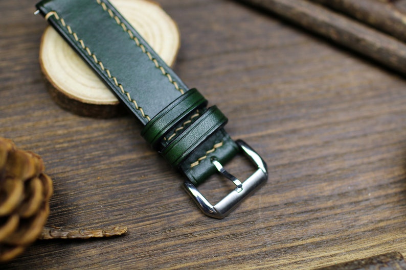 May include: A dark green leather watch strap with light brown stitching and a silver buckle.