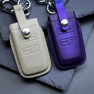 May include: Two leather key fobs with metal key rings. One fob is beige with a silver button and the other is purple with a silver button. Both fobs have multiple buttons with the word "EDGE" printed on them.