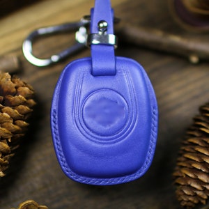 May include: A blue leather key fob with a silver loop and a stitched design. The fob is on a wooden surface.