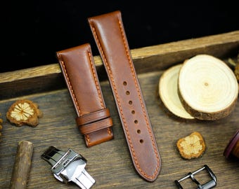 May include: Two brown leather watch straps with orange stitching, a silver watch clasp, and a black watch buckle are displayed on a wooden surface. The straps are new and unused. The background includes wood slices and decorative elements.