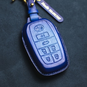 May include: A blue leather key fob with multiple buttons. The fob has a silver metal ring for attaching to a keychain.