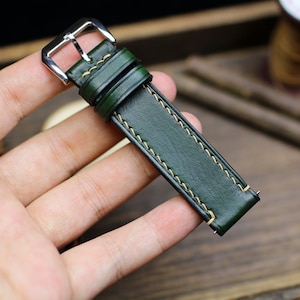 May include: A dark green leather watch strap with a silver buckle and yellow stitching.