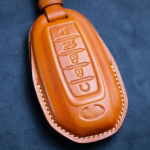 May include: A brown leather key fob with stitching around the edges. The fob has five buttons with raised symbols.