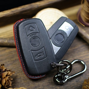 Puede incluir: Un llavero de cuero negro con costuras rojas y una cadena plateada. El llavero tiene botones con las etiquetas "Lock" y "Unlock".