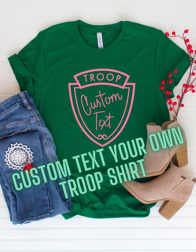Puede incluir: Camiseta verde con un dise&ntilde;o de escudo rosa que dice "TROOP Custom Text". El texto "CUSTOM TEXT YOUR OWN TROOP SHIRT" est&aacute; escrito en verde debajo del escudo.