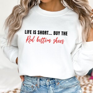 Pu&ograve; includere: Felpa bianca con il testo "Life is short... Buy the Red bottom shoes" in lettere nere e rosse.