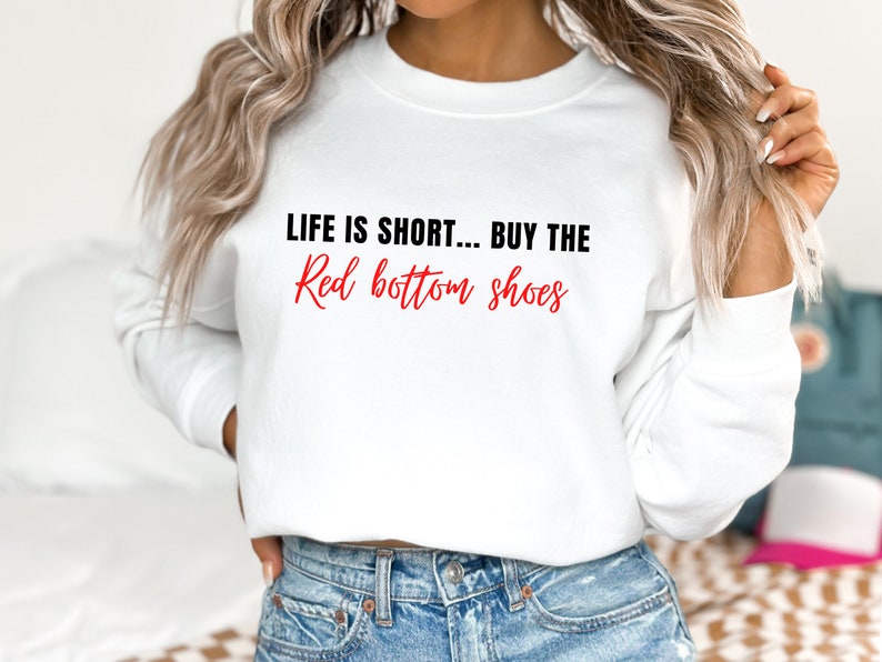 Pu&ograve; includere: Felpa bianca con il testo "Life is short... Buy the Red bottom shoes" in lettere nere e rosse.