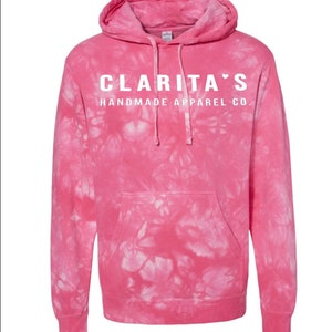 Puede incluir: Sudadera con capucha de color rosa tie-dye con texto blanco que dice "Clarita's Handmade Apparel Co."
