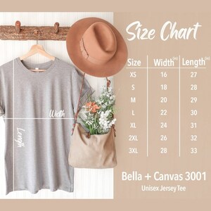K&ouml;nnte beinhalten: Eine Gr&ouml;&szlig;entabelle f&uuml;r ein Unisex-Jersey-T-Shirt, die die Breite und L&auml;nge in Zoll f&uuml;r die Gr&ouml;&szlig;en XS bis 3XL zeigt. Die Tabelle wird auf einem wei&szlig;en Hintergrund mit einem grauen T-Shirt angezeigt, das an einem Holzast h&auml;ngt, einem braunen Hut und einer braunen Tasche mit Blumen.