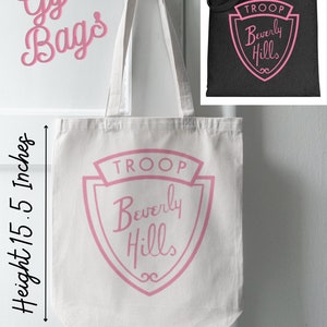 Puede incluir: Bolsa de lona blanca con letras rosas que dicen "TROOP Beverly Hills" en forma de escudo. La bolsa mide 14,5 pulgadas de ancho y 15,5 pulgadas de alto.