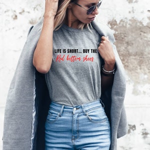 Pu&ograve; includere: Una maglietta grigia con la scritta "Life is short... Buy the Red bottom shoes" stampata sul davanti.