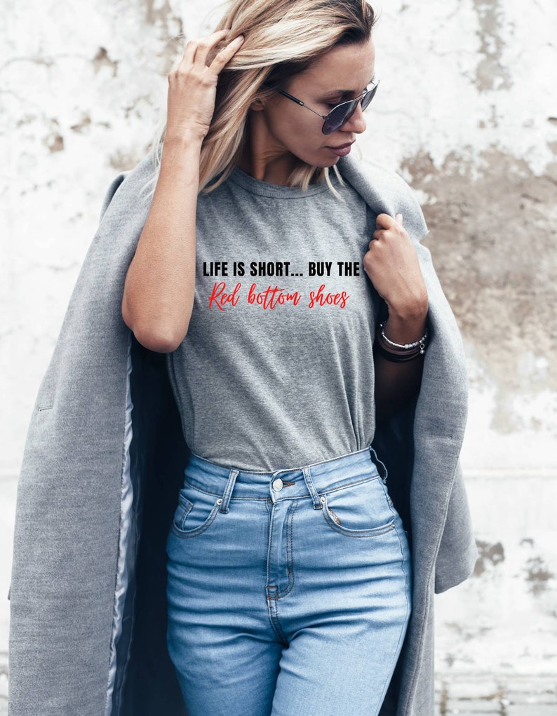Pu&ograve; includere: Una maglietta grigia con la scritta "Life is short... Buy the Red bottom shoes" stampata sul davanti.