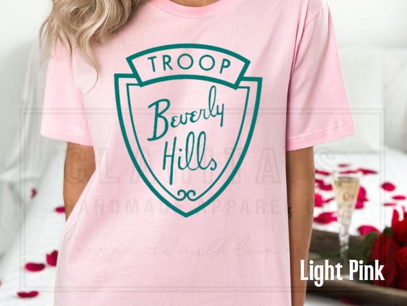 Puede incluir: Camiseta rosa claro con un gr&aacute;fico de escudo verde que dice "Troop Beverly Hills".