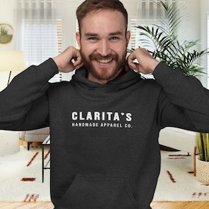 May include: A dark gray hooded sweatshirt with the text "CLARITA'S HANDMADE APPAREL CO." in white.