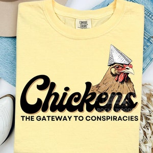 May include: A yellow t-shirt with a black graphic of a chicken wearing a tinfoil hat. The text "Chickens The Gateway to Conspiracies" is printed below the chicken.