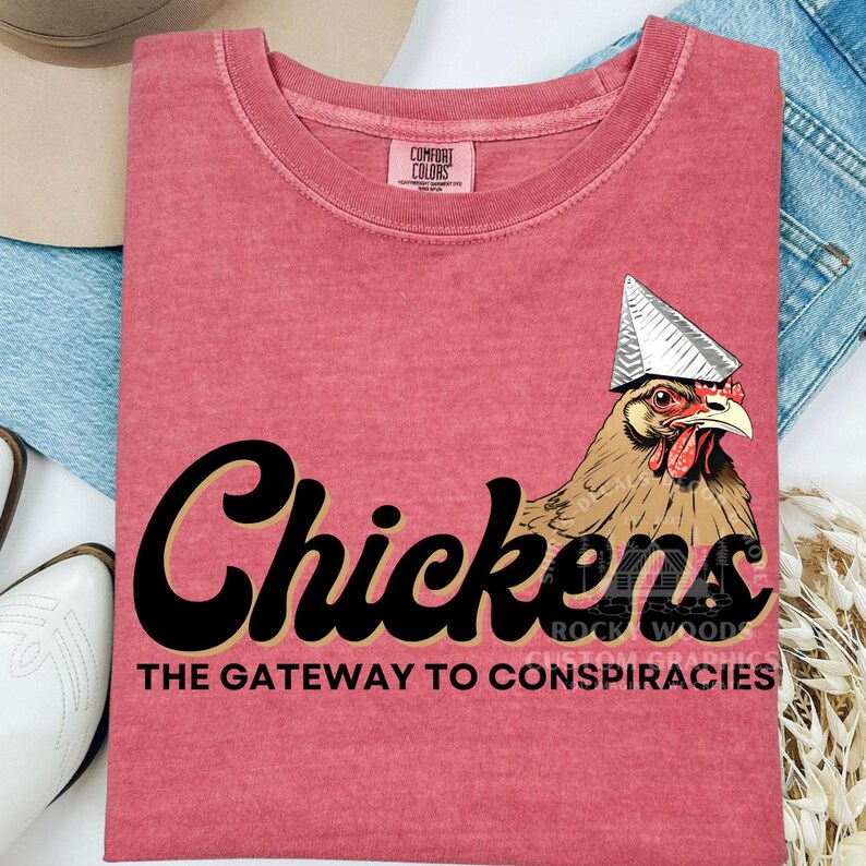 May include: A red t-shirt with a black graphic of a chicken wearing a tinfoil hat. The text "Chickens The Gateway to Conspiracies" is printed below the graphic.