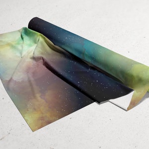 Puede incluir: Un rollo de tela con estampado de galaxia que presenta un fondo azul oscuro con estrellas blancas y un degradado de verde, amarillo y naranja.