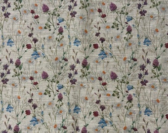May include: A beige fabric with a repeating pattern of small blue, purple, and white flowers. The fabric has a subtle texture.
