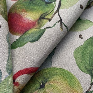 May include: A close-up of a fabric with a repeating pattern of green leaves and red apples on a light gray background.