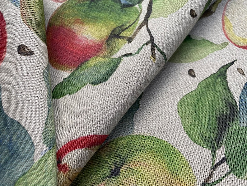 May include: A close-up of a fabric with a repeating pattern of green leaves and red apples on a light gray background.